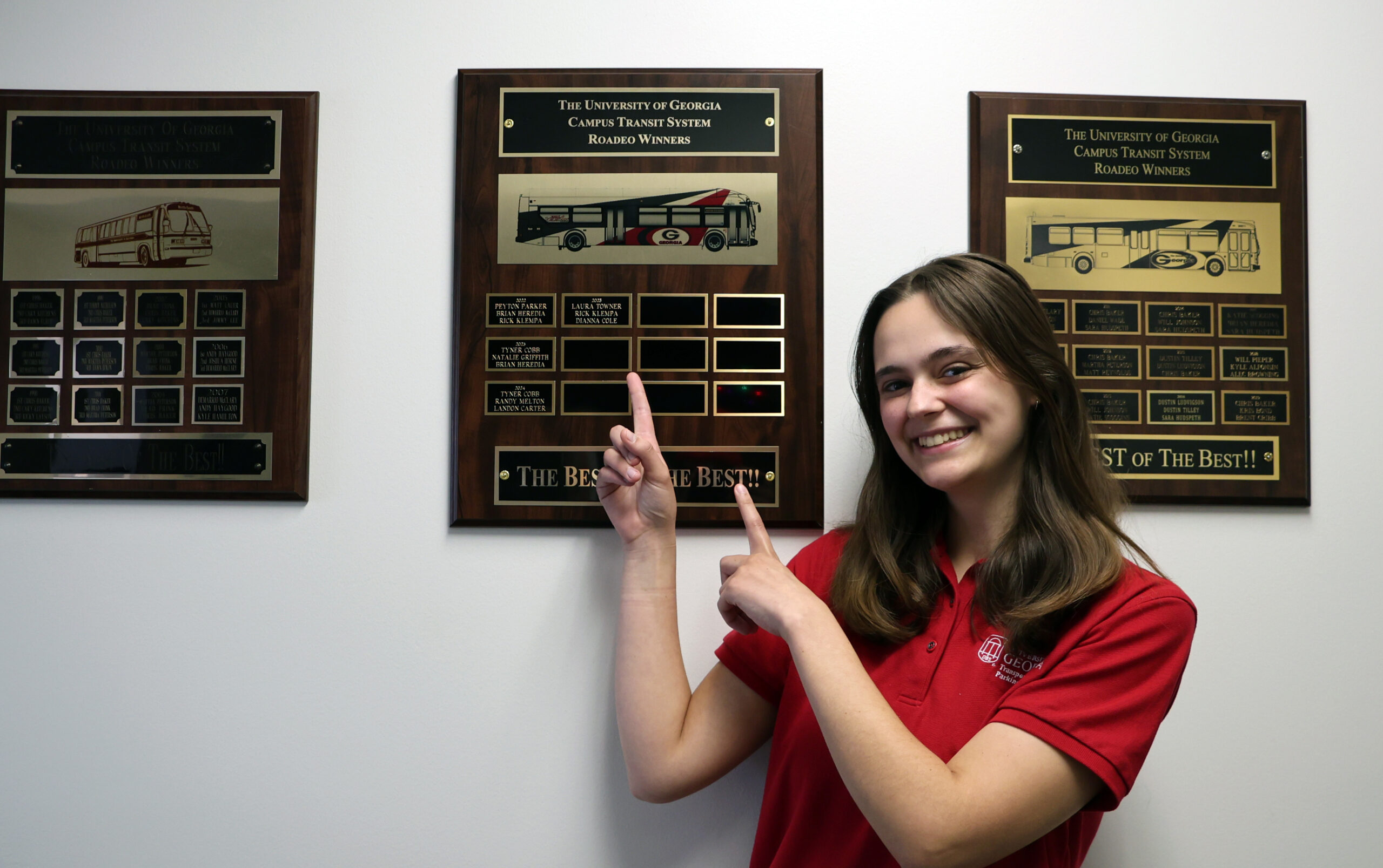 Student bus driver pointing to plaque on wall