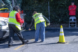 People measuring distance between bus and traffic cone