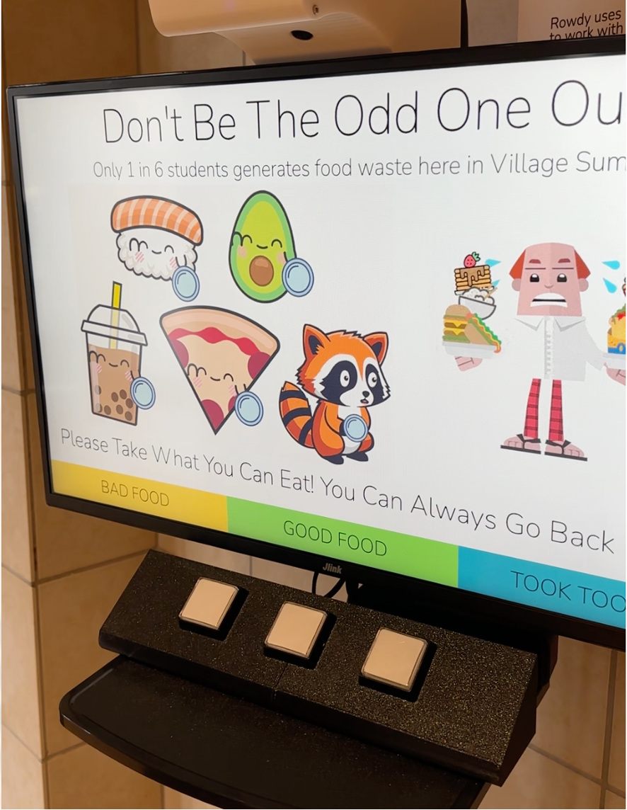 Raccoon eyes kiosk in the dining commons. The screen shows a cartoon raccoon, food items, and a man holding plates of food in his hands and invites customers to leave feedback.