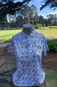 Women's golf shirt with University of Georgia logo on it shown outside with the UGA golf course in the background